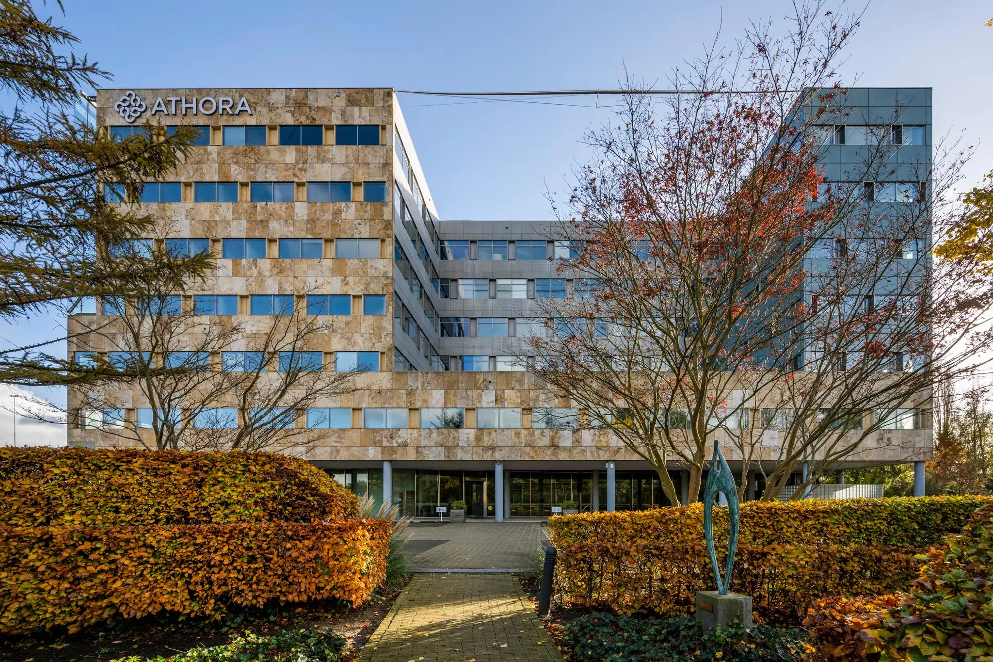 Vooraanzicht van het kantoorgebouw van Athora aan de Burgemeester Rijnderslaan, omgeven door herfstige beplanting.